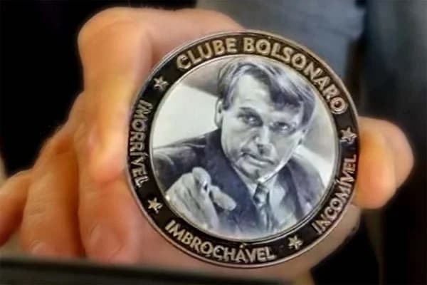 Uma medalha com o rosto do genocida referente a uma piada feita para a plateia bovina do cercadinho